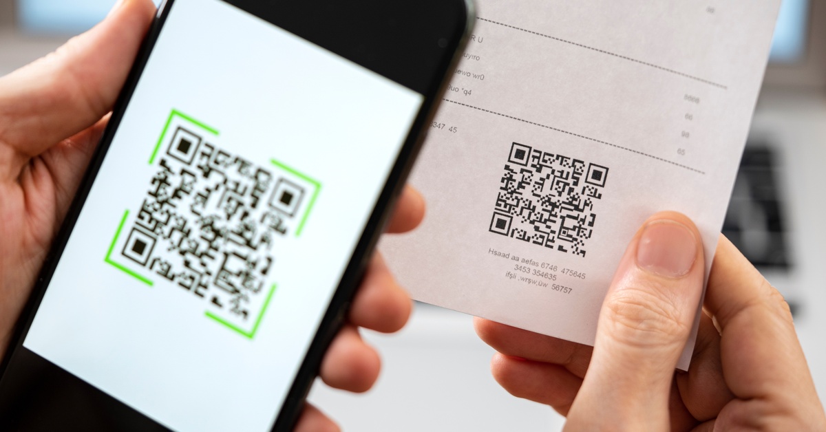 A close-up of a person taking a photo of a QR code with their smartphone. The QR code is at the bottom of a receipt.