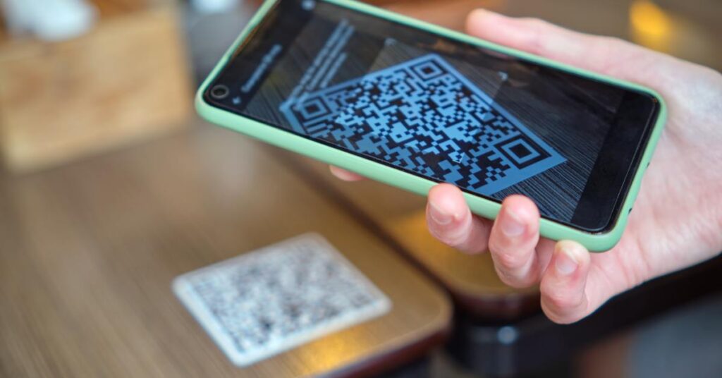 A close-up of a restaurant customer scanning the QR code taped to the table. They have a green phone case.