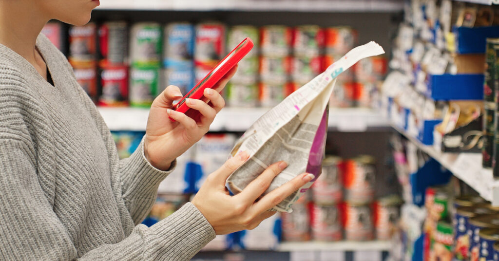 A consumer stands in the grocery store aisle as they use their phone to scan a product packaging label.
